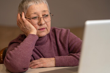 A senior woman sitting in front of a laptop communicates online through social networks.