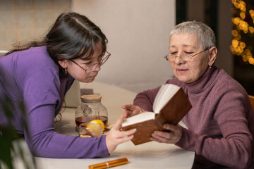 grandmother and granddaughter drink tea sitting at the table and read a book.