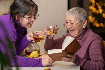 grandmother and granddaughter drink tea sitting at the table and read a book.