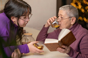 grandmother and granddaughter drink tea sitting at the table and read a book.