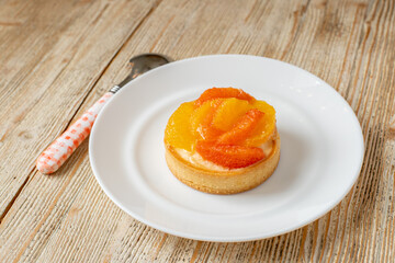 Tartlet with tangerine and grapefruit lies on a plate on a wooden table. beautiful dessert