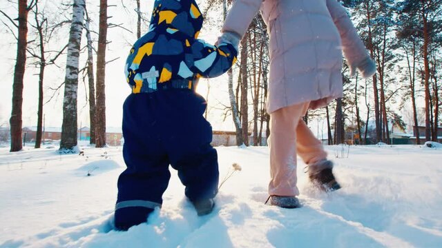 Winter family fun. Young mother runs with her toddler kid in the winter garden