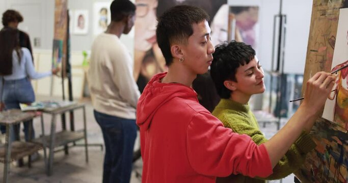 Multiracial students painting together inside art classroom at university