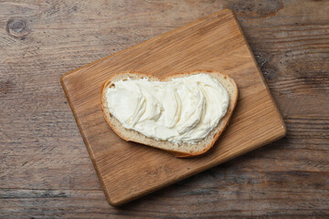Slice of bread with tasty cream cheese on wooden table, top view