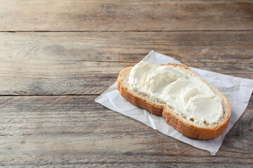 Slice of bread with tasty cream cheese on wooden table, space for text