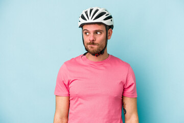 Young caucasian man with bike helmet isolated on blue background confused, feels doubtful and unsure.