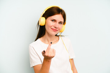 Young English woman listening to music isolated on blue background pointing with finger at you as if inviting come closer.