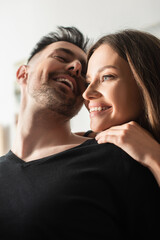 low angle view of happy young woman embracing laughing boyfriend in bedroom.