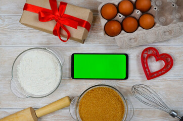 red festive ingrediens for cooking, valentines day eggs, rolling pin and whisk, cutter dish shape heart for baking cake flat lay, chroma key smart phone copy space