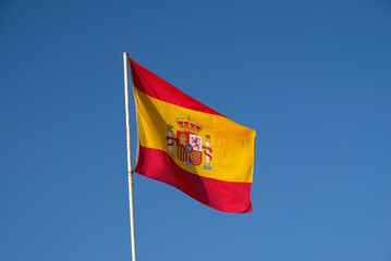 Spanish national flag waving on blue sky background. The flag on a flagpole flutters in the wind. Red with yellow Spain Flag blowing in the wind against on blue sky