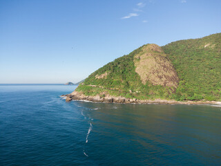 Fototapeta premium Aerial view of Prainha Beach, a paradise in the west side of Rio de Janeiro, Brazil. Big hills around. Sunny day at dawn. Greenish sea. Drone Photo