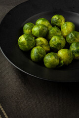 Overhead view of frozen brussels sprouts on black plate and dark cloth, selective focus, vertical, with copy space