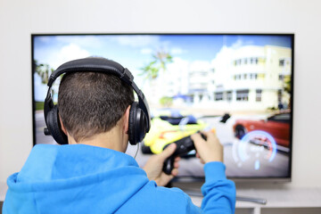 Guy in headphones playing with a gamepad a racing video game on TV screen. Concept of game...