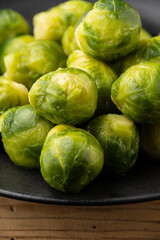 Close-up of brussels sprouts on black plate on rustic wooden table, selective focus, vertical