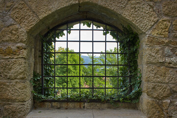 grated window in an old stone wall with a landscape in the background. Close-up
