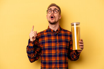 Young caucasian man holding spaghettis jar isolated on yellow background pointing upside with opened mouth.