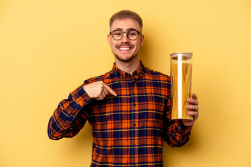 Young caucasian man holding spaghettis jar isolated on yellow background person pointing by hand to a shirt copy space, proud and confident