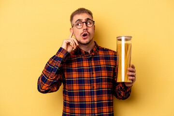 Young caucasian man holding spaghettis jar isolated on yellow background trying to listening a gossip.