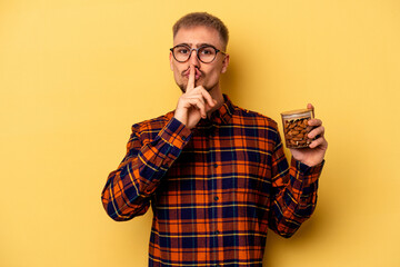 Young caucasian man holding a almond jar isolated on yellow background keeping a secret or asking...