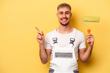 Young painter man isolated on yellow background smiling and pointing aside, showing something at...