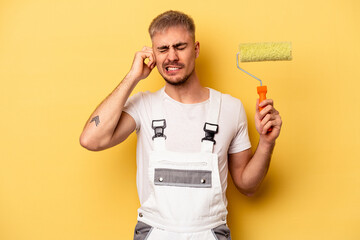 Young painter man isolated on yellow background covering ears with hands.