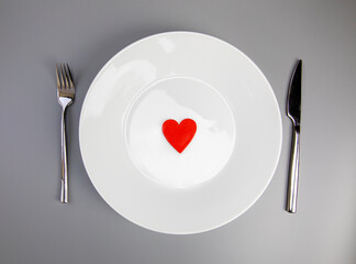 White plate with, fork and knife, red heart on grey background, flat lay. Valentine's day or medical health concept top view
