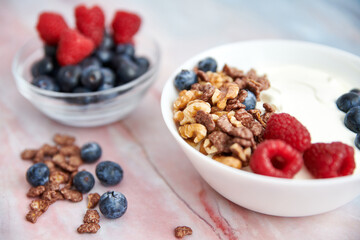 Bowl with Greek yogurt, nuts, cereals, blueberries and fresh raspberries on a marble background