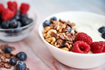 Bowl with Greek yogurt, nuts, cereals, blueberries and fresh raspberries on a marble background