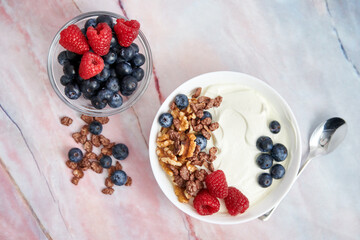 Bowl with Greek yogurt, nuts, cereals, blueberries and fresh raspberries on a marble background. top view