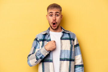 Young caucasian man isolated on yellow background surprised pointing with finger, smiling broadly.