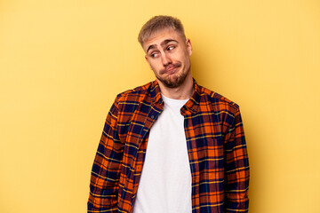 Young caucasian man isolated on yellow background shrugs shoulders and open eyes confused.