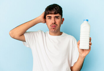 Young mixed race man holding a bottle of milk isolated on blue background being shocked, she has remembered important meeting.