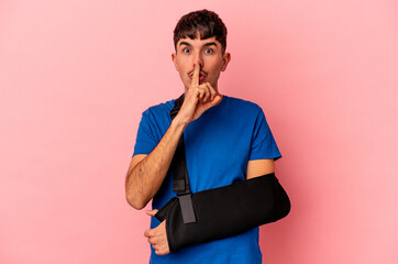 Young mixed race man with broken hand isolated on pink background keeping a secret or asking for silence.