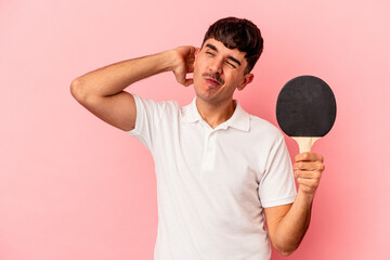 Young mixed race man holding a ping pong racket isolated on pink background touching back of head,...