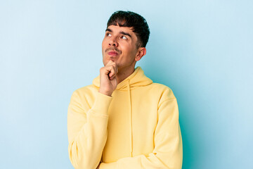 Young mixed race man isolated on blue background thinking and looking up, being reflective, contemplating, having a fantasy.