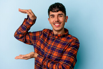 Naklejka premium Young mixed race man isolated on blue background holding something little with forefingers, smiling and confident.
