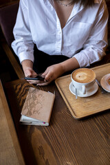 Fototapeta na wymiar Young woman typing message on mobile phone while drinking coffee. Businesswoman keeps social distance