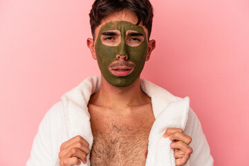 Young mixed race man wearing beauty facial mask isolated on pink background