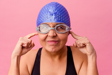 Young swimmer covers ears, focused on peaceful silence while wearing cap and goggles.