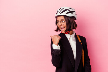 Young business mixed race woman wearing a bike helmet isolated on pink background points with thumb finger away, laughing and carefree.