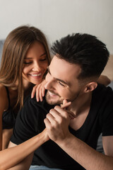 happy young couple holding hands and smiling in bedroom.