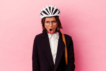 Young business mixed race woman wearing a bike helmet isolated on pink background screaming very angry and aggressive.