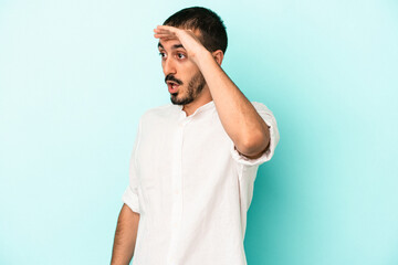 Young caucasian man isolated on blue background looking far away keeping hand on forehead.