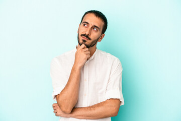 Young caucasian man isolated on blue background looking sideways with doubtful and skeptical expression.