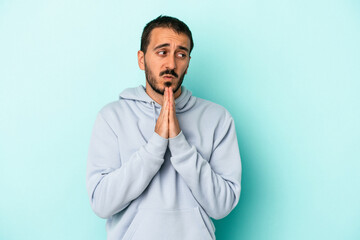Fototapeta premium Young caucasian man isolated on blue background praying, showing devotion, religious person looking for divine inspiration.