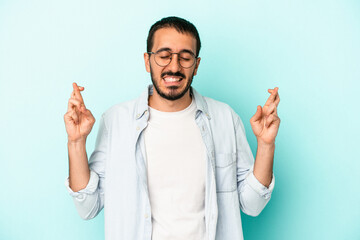 Naklejka premium Young caucasian man isolated on blue background crossing fingers for having luck