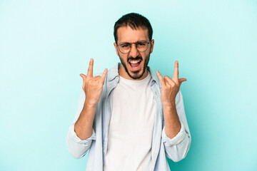 Fototapeta premium Young caucasian man isolated on blue background showing a horns gesture as a revolution concept.
