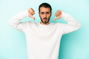 Young caucasian man isolated on blue background showing a dislike gesture, thumbs down....