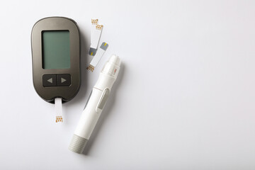 Digital glucometer, lancet pen and test strips on white background, flat lay with space for text. Diabetes control