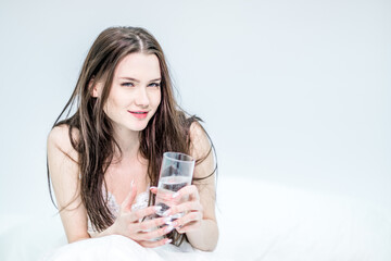 A woman is sitting in bed with a glass of water in her hands. Good habits. Healthy lifestyle.